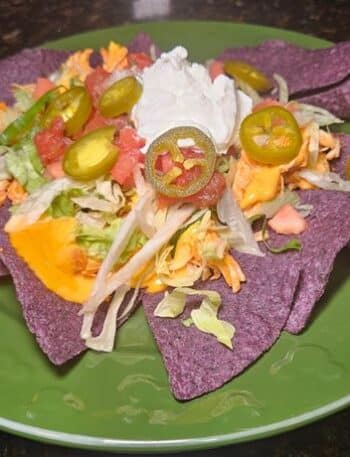 Disney Hades Nachos Recipe: Blue corn tortilla chips topped with buffalo chicken, queso, lettuce, tomato, salsa, sour cream, and jalapenos