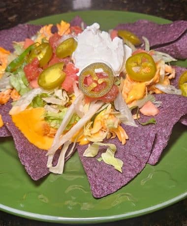 Disney Hades Nachos Recipe: Blue corn tortilla chips topped with buffalo chicken, queso, lettuce, tomato, salsa, sour cream, and jalapenos