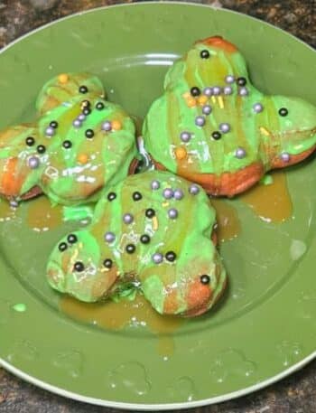 Disneyland Caramel Apple Beignets Recipe: 3 Beignets arranged on a green plate with hidden Mickey's. Beignets are topped with a green apple candy icing and Halloween sprinkles.