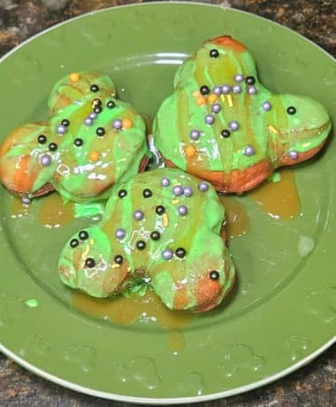 Disneyland Caramel Apple Beignets Recipe: 3 Beignets arranged on a green plate with hidden Mickey's. Beignets are topped with a green apple candy icing and Halloween sprinkles.