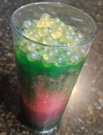 Night Blossom Animal Kingdom Recipe: a clear plastic cup is filled with 3 layers: green, neon pink, and green again topped with popping boba.