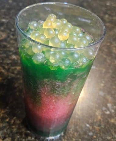 Night Blossom Animal Kingdom Recipe: a clear plastic cup is filled with 3 layers: green, neon pink, and green again topped with popping boba.