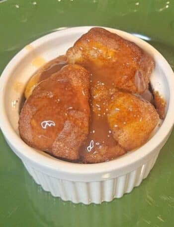 Disneyland Pumpkin Spice Monkey Bread Recipe: A white ramekin on a green plate filled with pieces of Pumpkin Spice Monkey Bread drizzled with caramel sauce.