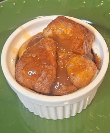Disneyland Pumpkin Spice Monkey Bread Recipe: A white ramekin on a green plate filled with pieces of Pumpkin Spice Monkey Bread drizzled with caramel sauce.