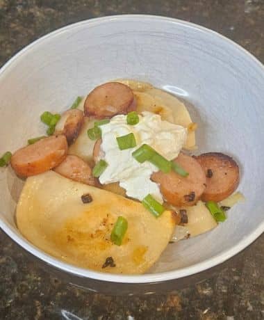 EPCOT Potato Pierogis Recipe: A bowl filled with 3 browned pierogis, browned kielbasa, sour cream, and chopped green onions