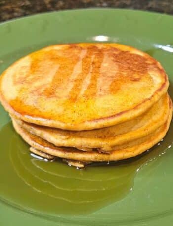 Kona Café Pumpkin Pancakes Recipe: 3 pancakes topped with maple syrup on a green plate with Mickey Mouse icons.