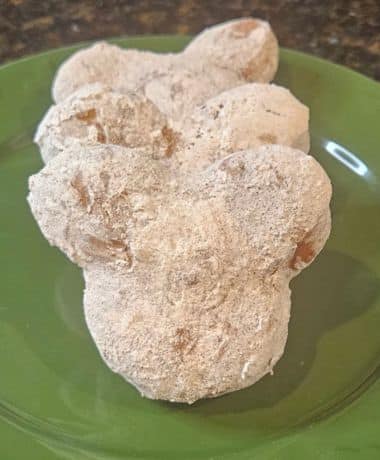 Pumpkin Spice Mickey Beignets Recipe: 3 Mickey Shaped Beignets on a green plate covered in pumpkin spice powdered sugar.